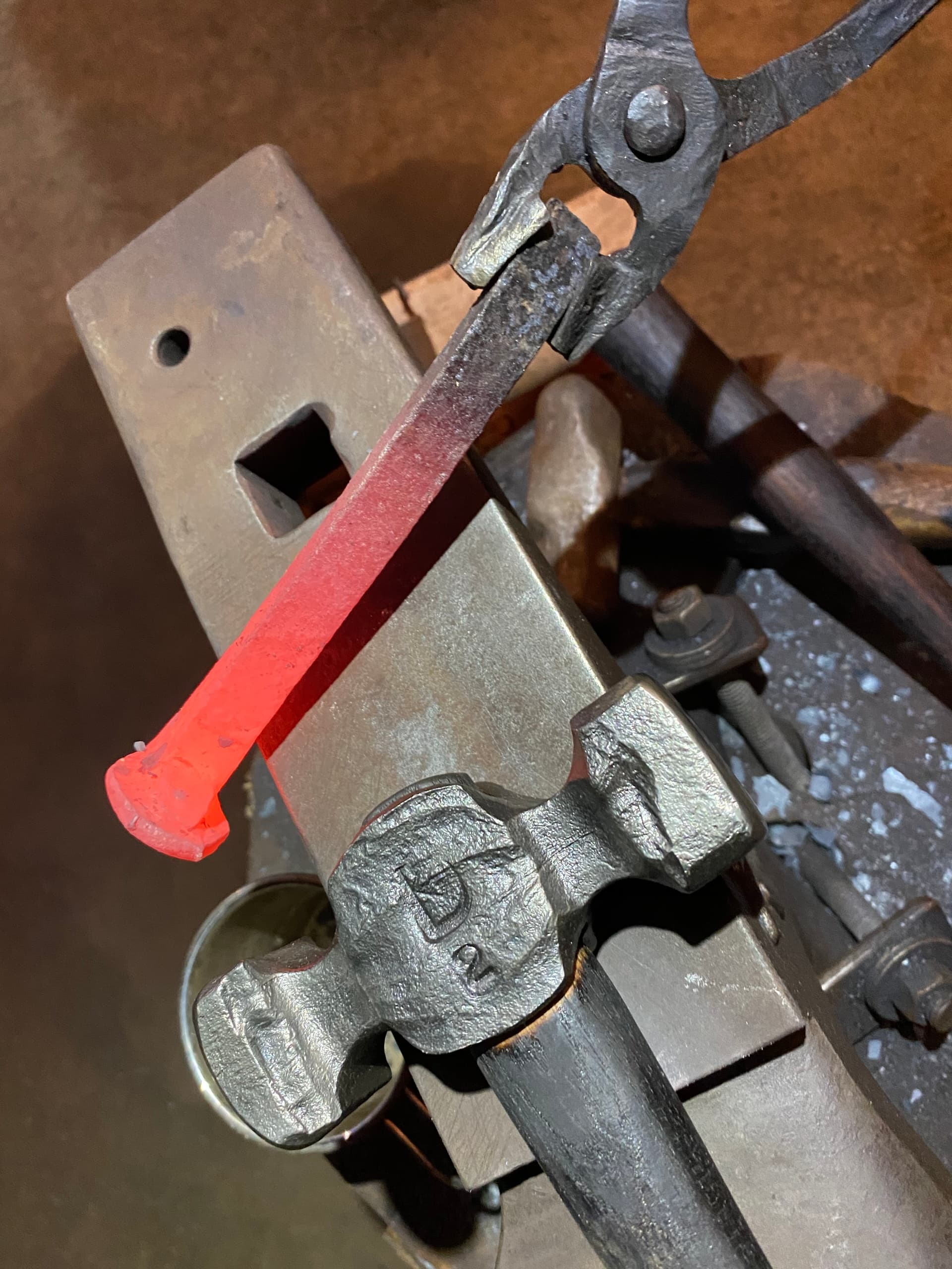Blacksmith heating red-hot steel held by tongs on anvil