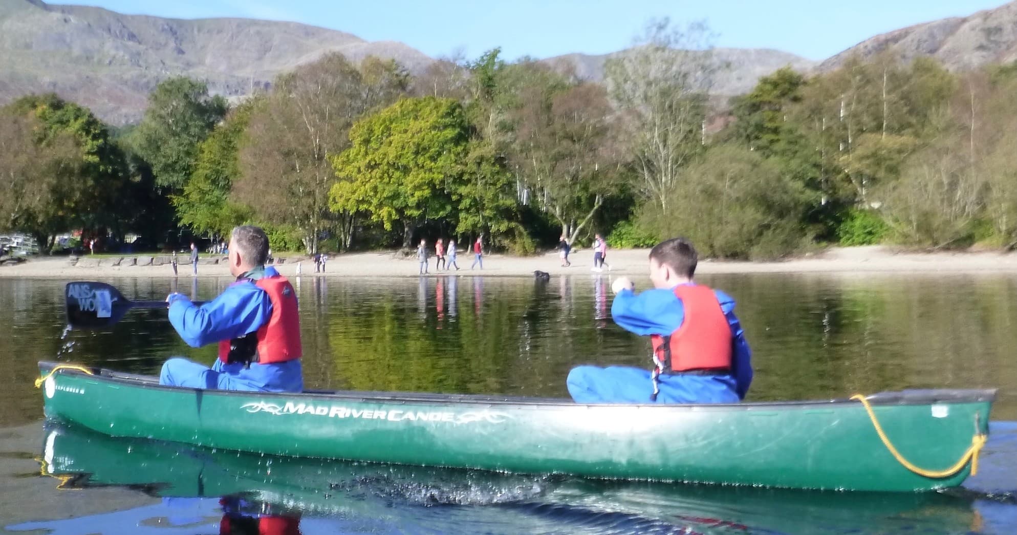 Two paddlers canoeing on tranquil lake with mountain backdrop