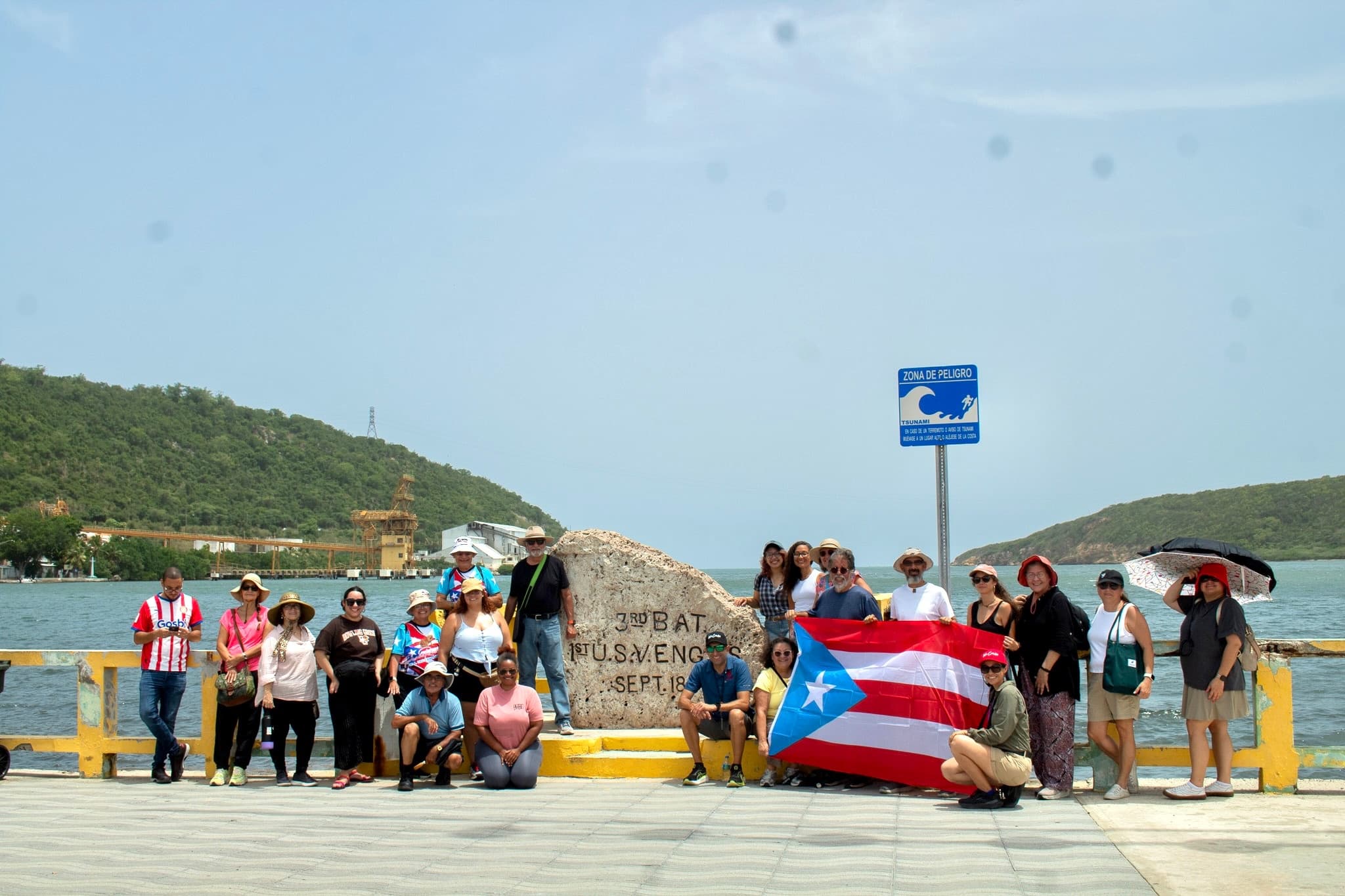 Tour group posing with Puerto Rico flag on coastal pier, island view