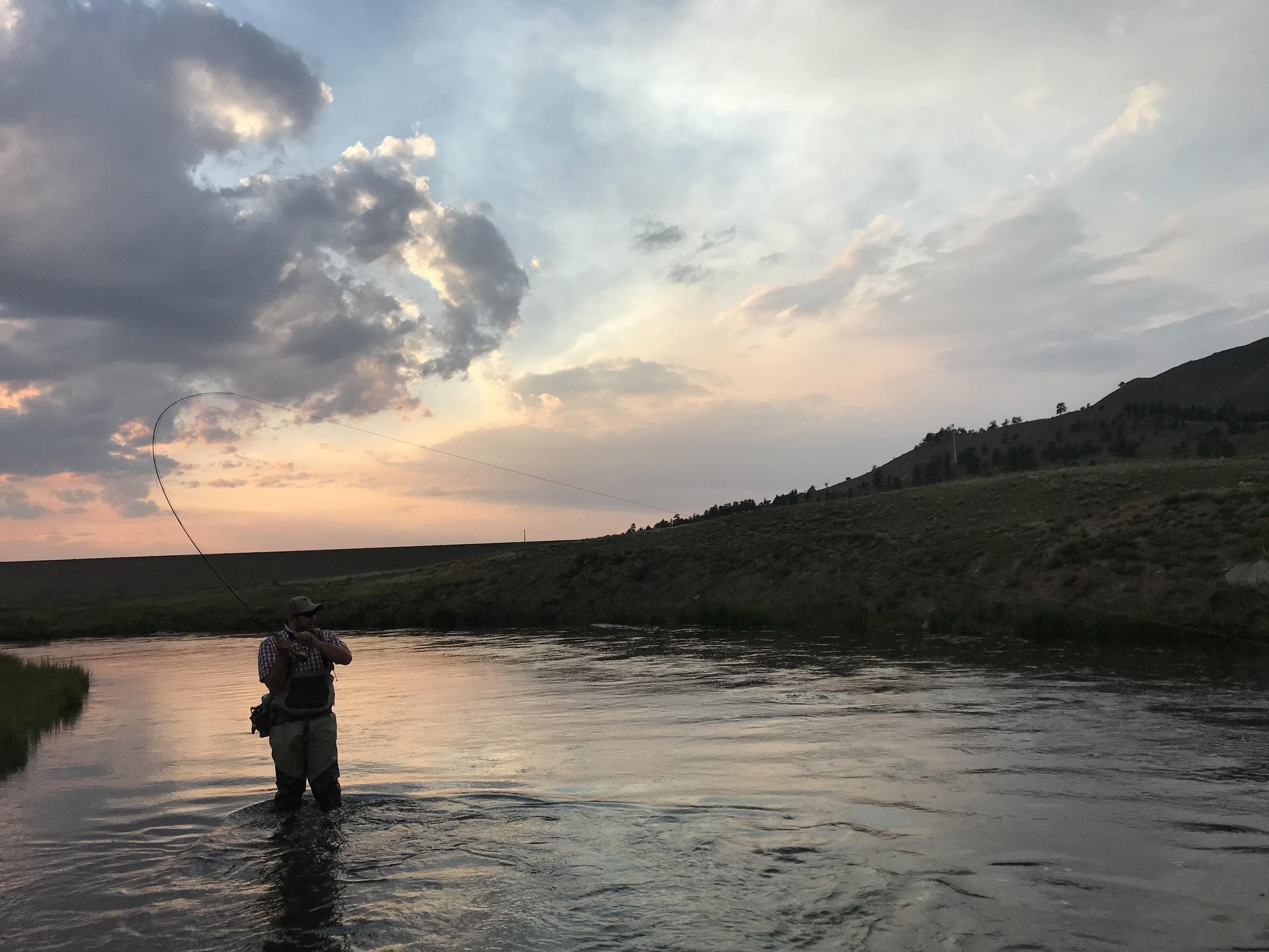 Silhouetted angler wading at sunset on wide prairie river