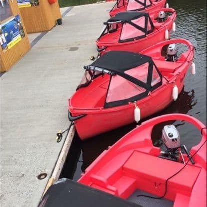 Red hire motorboats moored at a lakeside dock for cruising