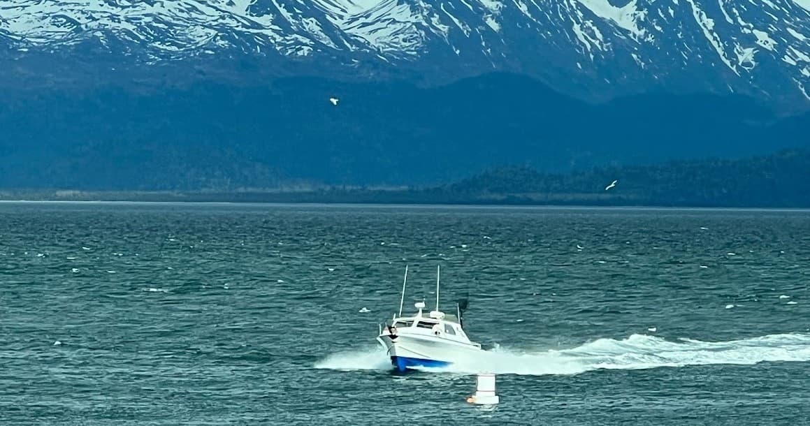 Charter fishing boat cruising coastal waters near snow-capped mountains