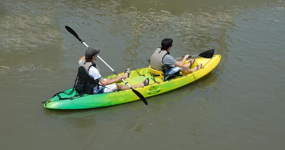 Two people kayaking on river in bright day, paddling together