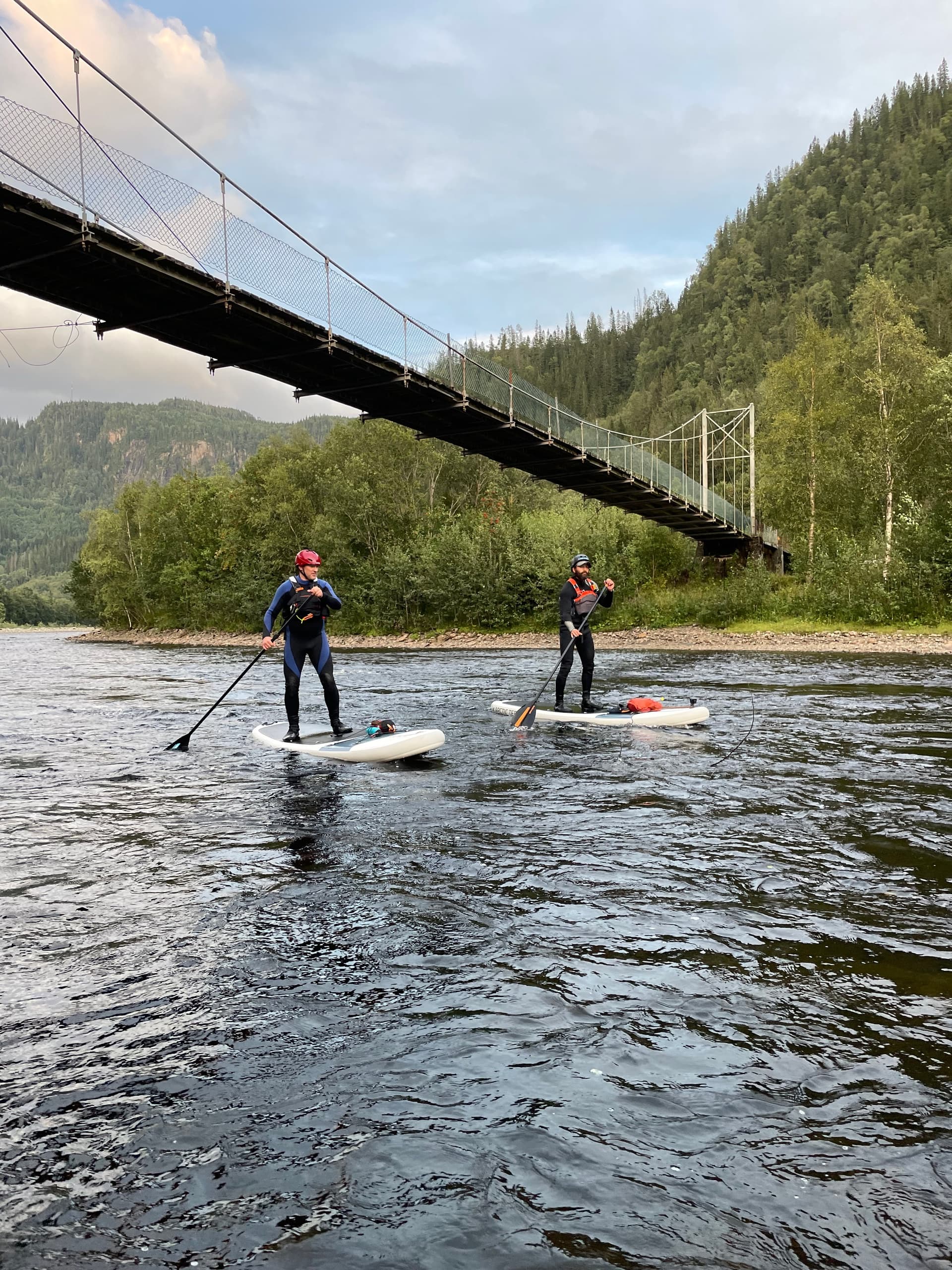 Two standup paddlers under suspension bridge on scenic mountain river