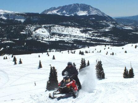 Snowmobile ride across snowy mountain basin with distant peaks