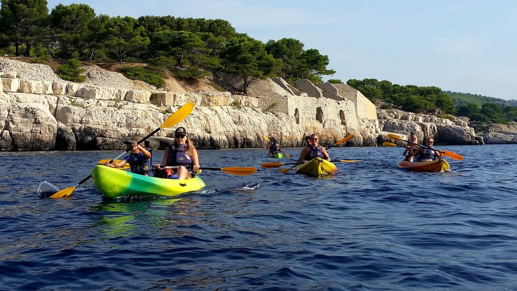 Group kayaking along rocky Mediterranean coast, guided sea tour