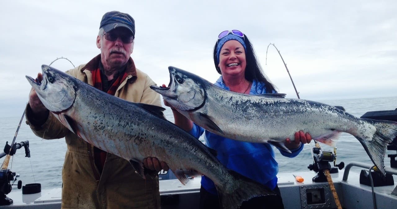 Anglers holding large salmon onboard charter boat at sea
