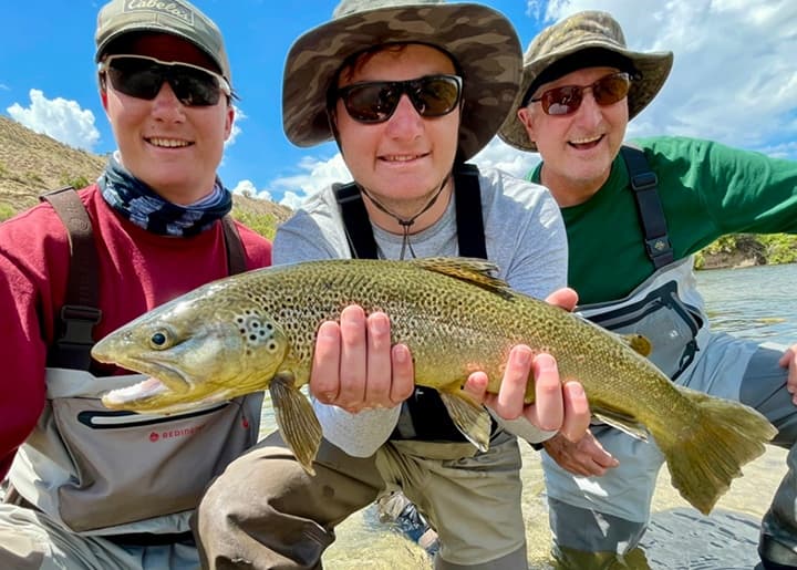 Group holding large brown trout during sunny river fishing trip
