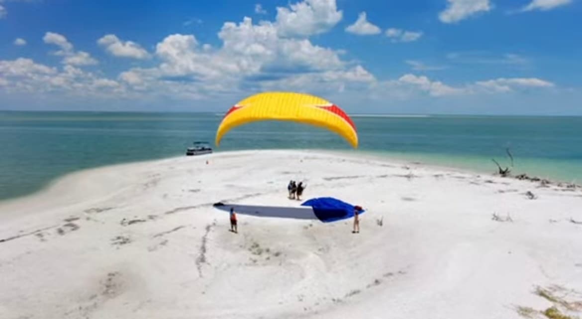 Paraglider canopy landed on white sandy beach by turquoise sea