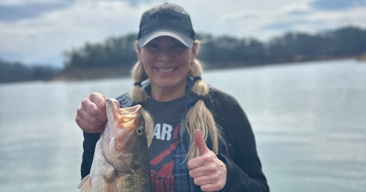 Woman angler holding large bass at lake shore, recreational fishing