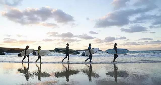 Surfers carrying boards across reflective beach at sunset