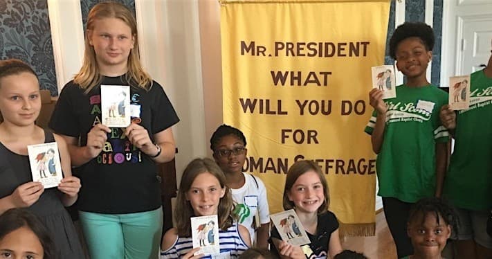 Kids holding suffrage postcards in museum program near banner