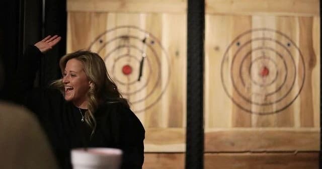 Woman axe throwing and high-fiving at indoor target lanes