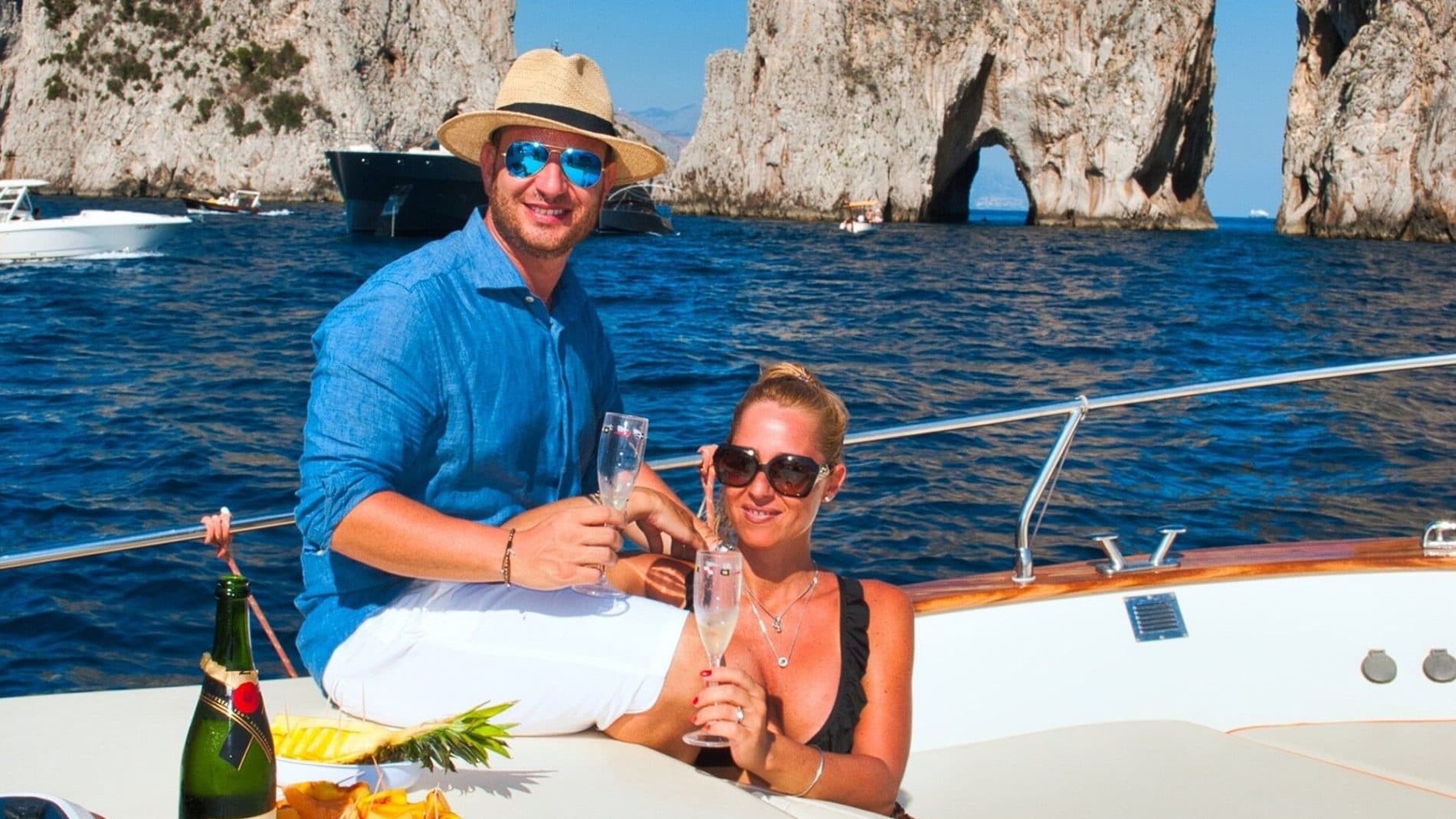 Couple relaxing under striped awning with sea arch views from boat