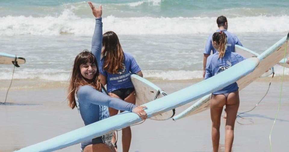 Happy surfers with boards walking on sandy beach before lesson