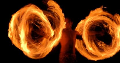 Fire knife dancer spinning flaming poi during night show