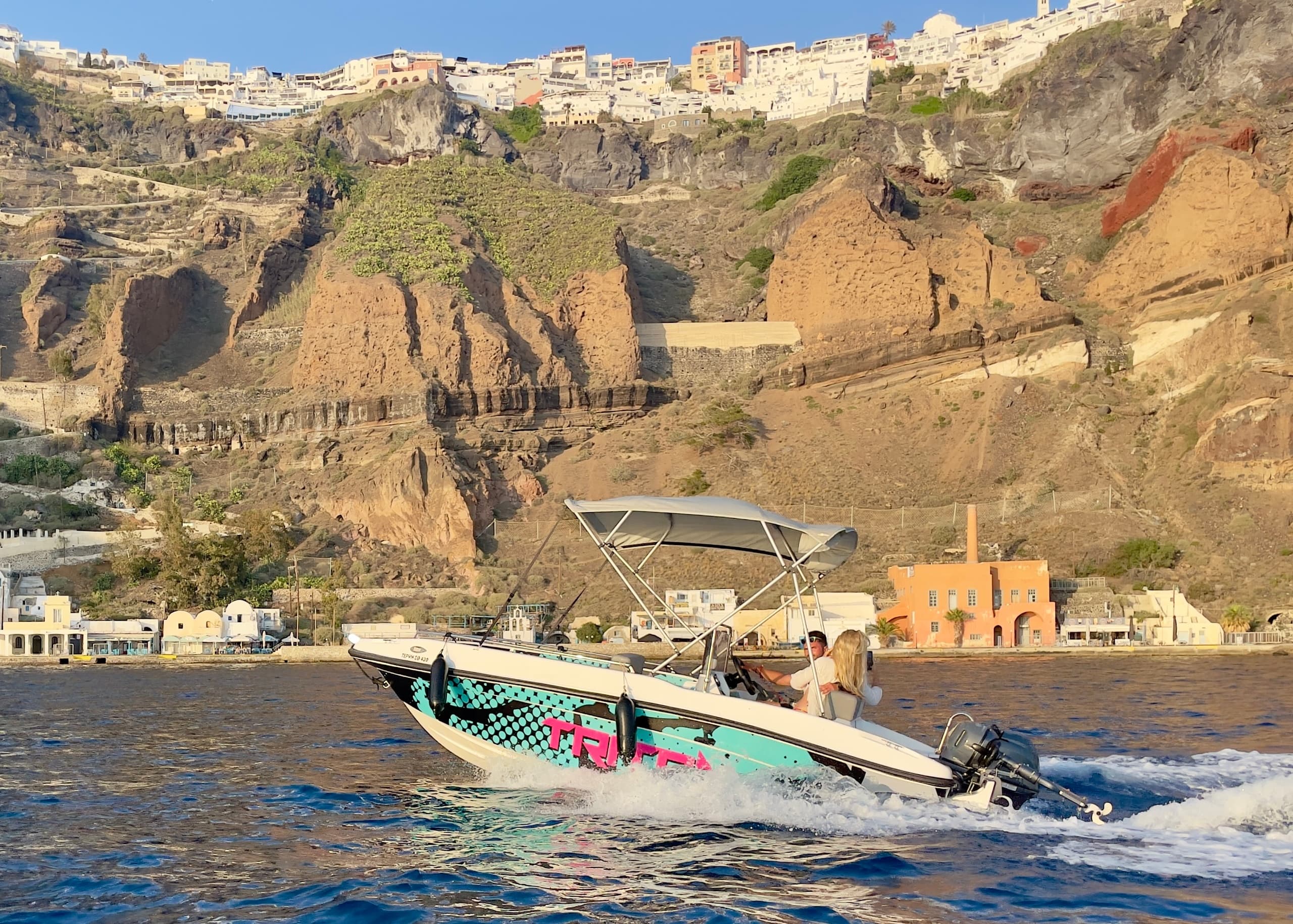 Speedboat cruising past cliffside village along coastal waters