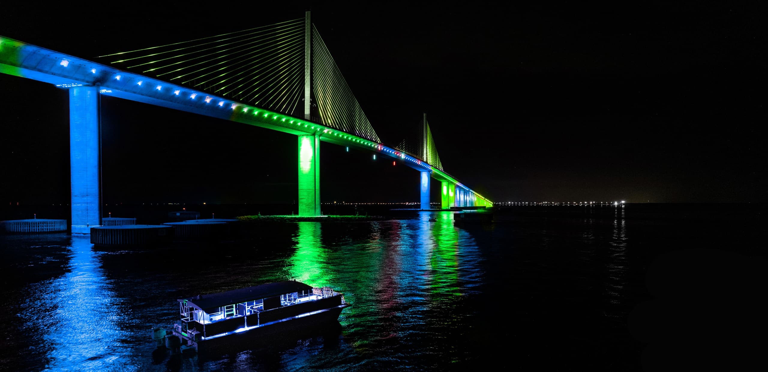 Night view of illuminated bridge spanning water with reflections