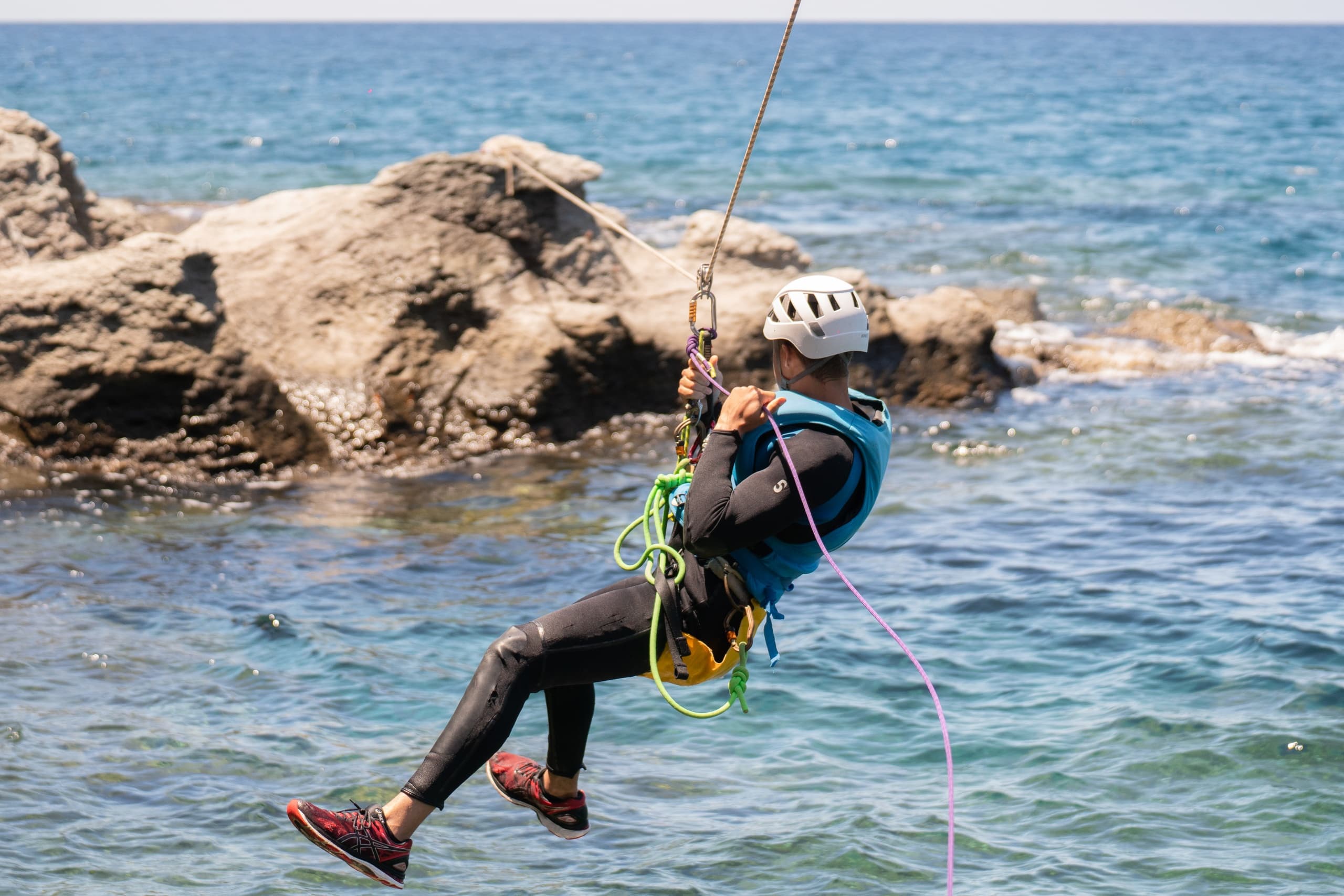 Rope descent over rocky coastal shoreline above blue sea