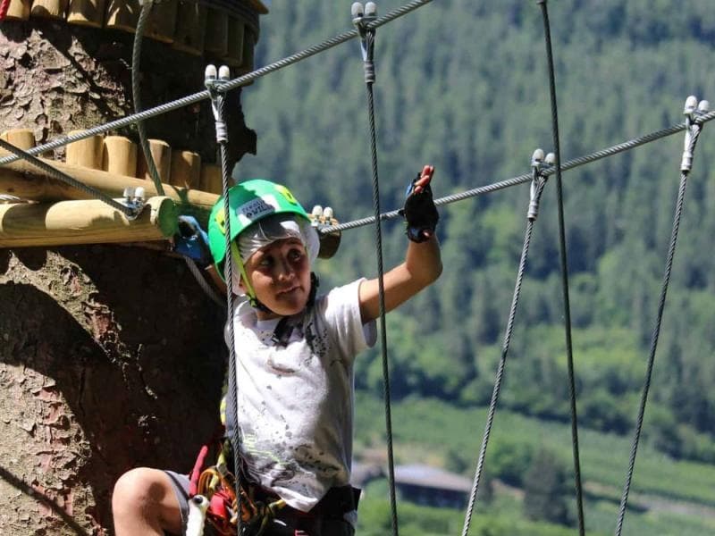 Child navigating high ropes course over forested valley in Marilleva