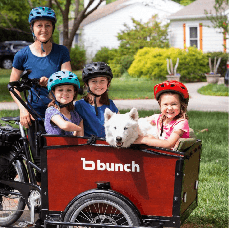 Family riding cargo e-bike with kids and dog on suburban street