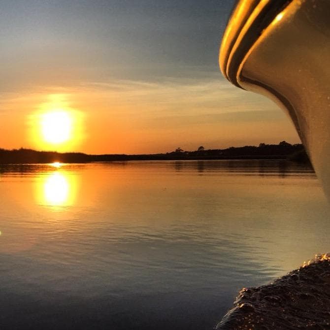 Sunset over calm coastal water from a boat bow at dusk