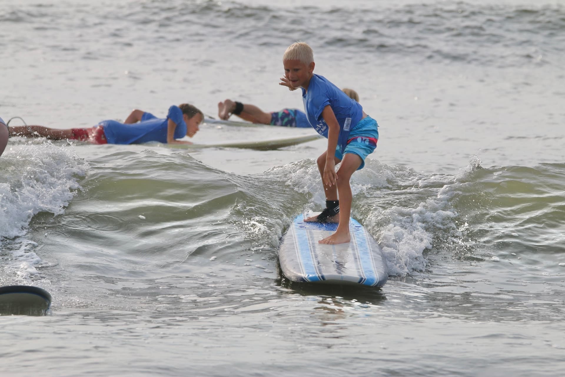 Child surfing small ocean wave on longboard at beach lesson