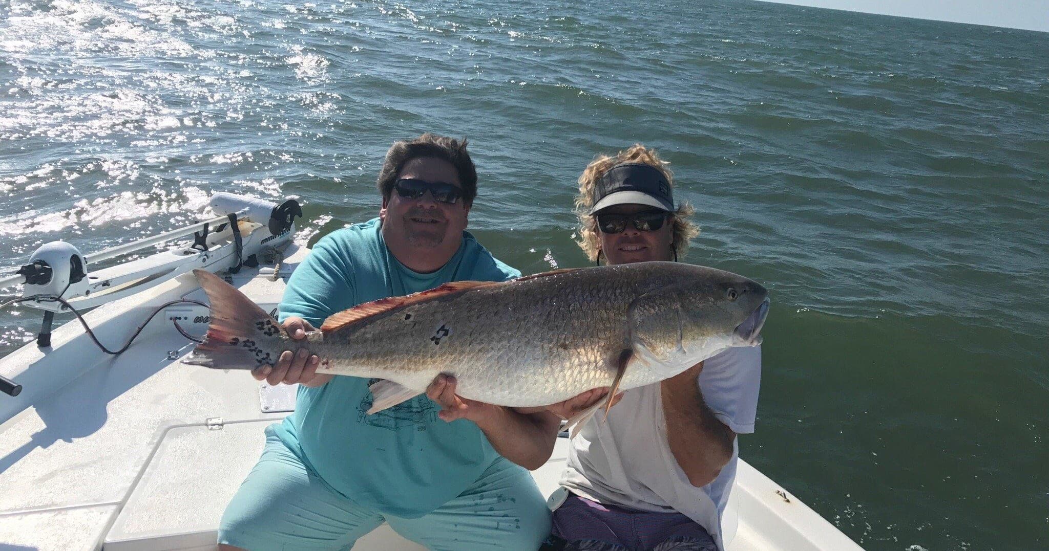 Two anglers holding big redfish aboard charter boat offshore