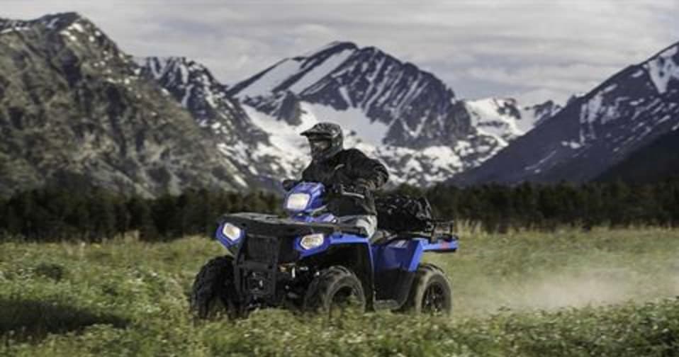 ATV traversing alpine meadow with snow-capped mountain vista