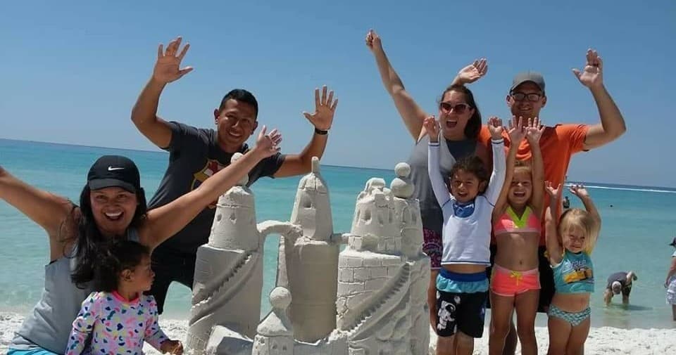 Smiling family beside detailed sandcastle at shoreline