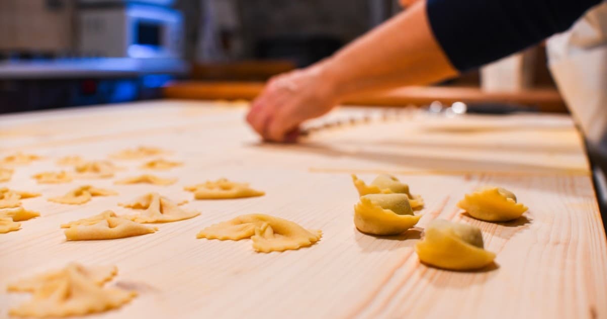 Handmade tortellini being shaped on wooden table in kitchen