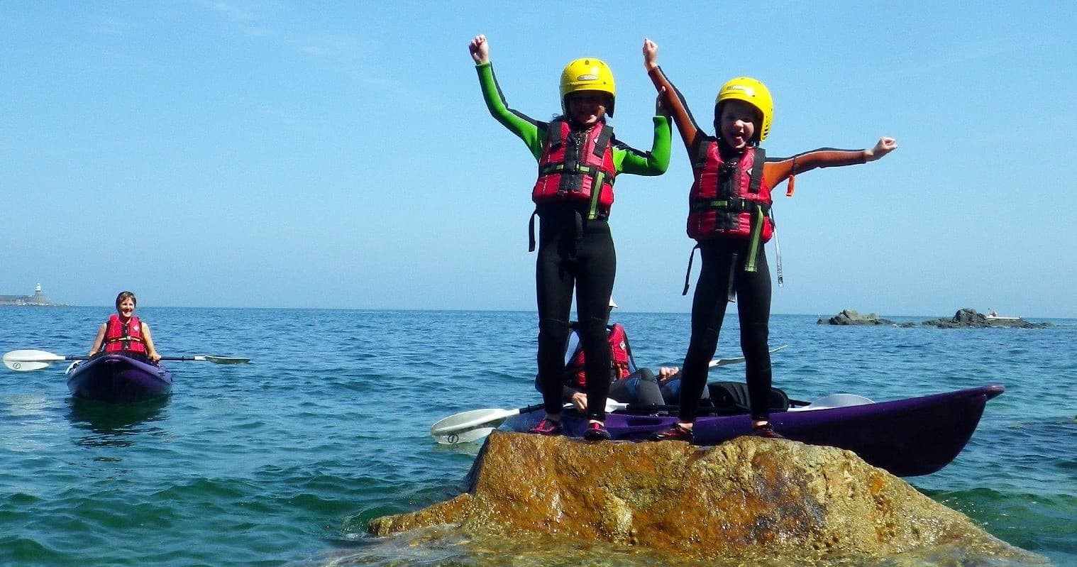 Two children standing on rock during coastal kayak trip