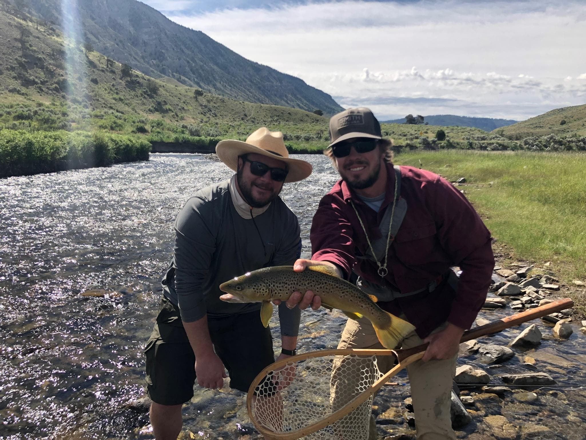 Anglers holding trout beside clear mountain stream on sunny day