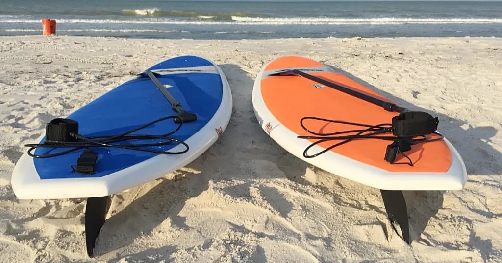 Two paddleboards resting on white sandy beach with ocean view
