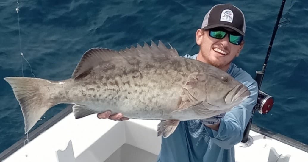 Angler holding large grouper on boat deck during offshore fishing trip
