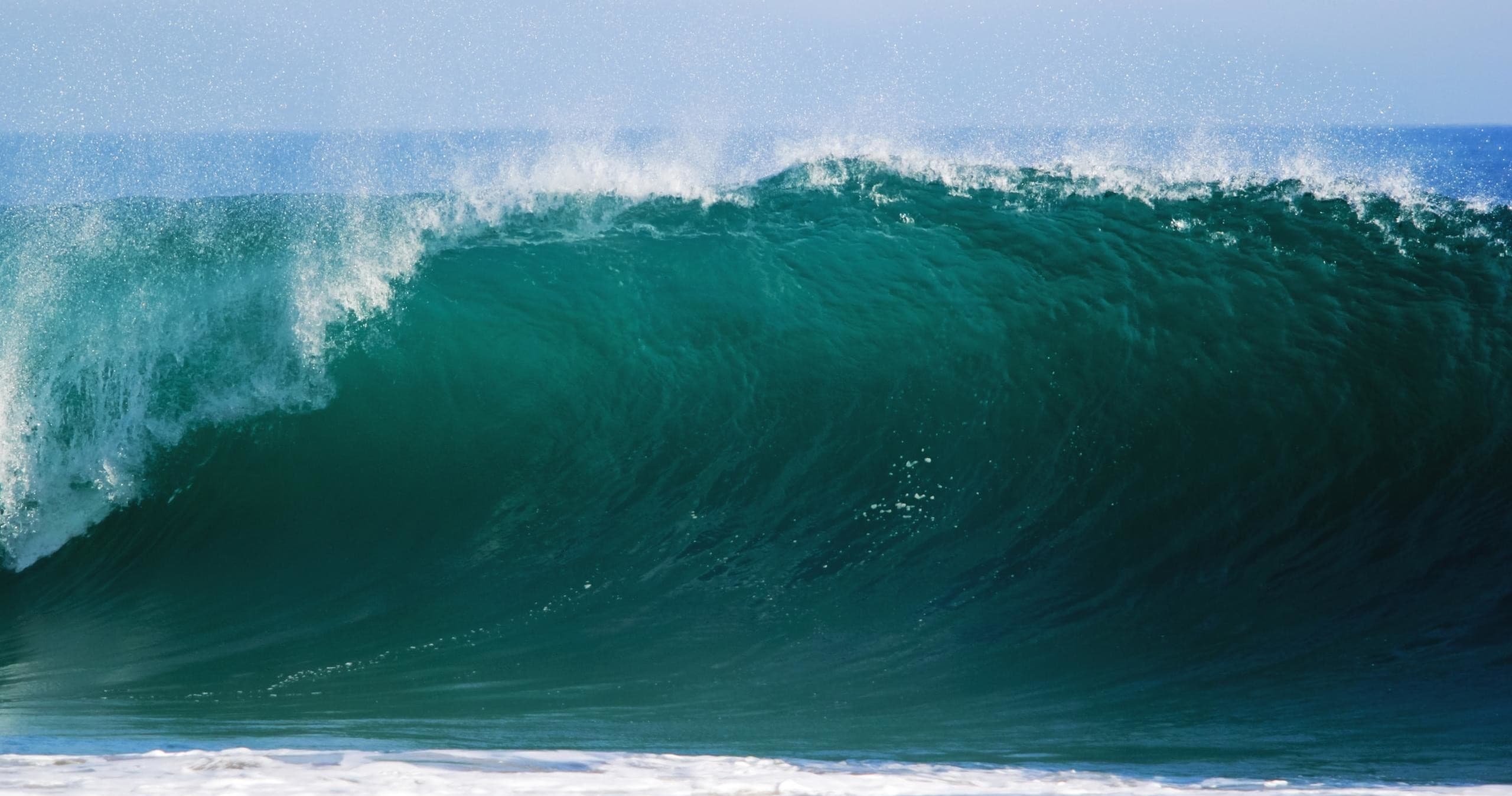 Massive teal ocean wave breaking over reef, surfing scene