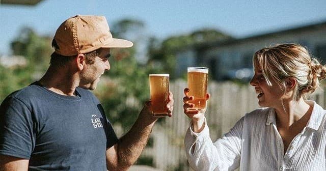 Couple toasting craft beers outdoors on a sunny brewery patio