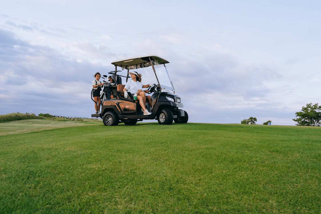 People riding a golf cart on grassy coastal course at sunset