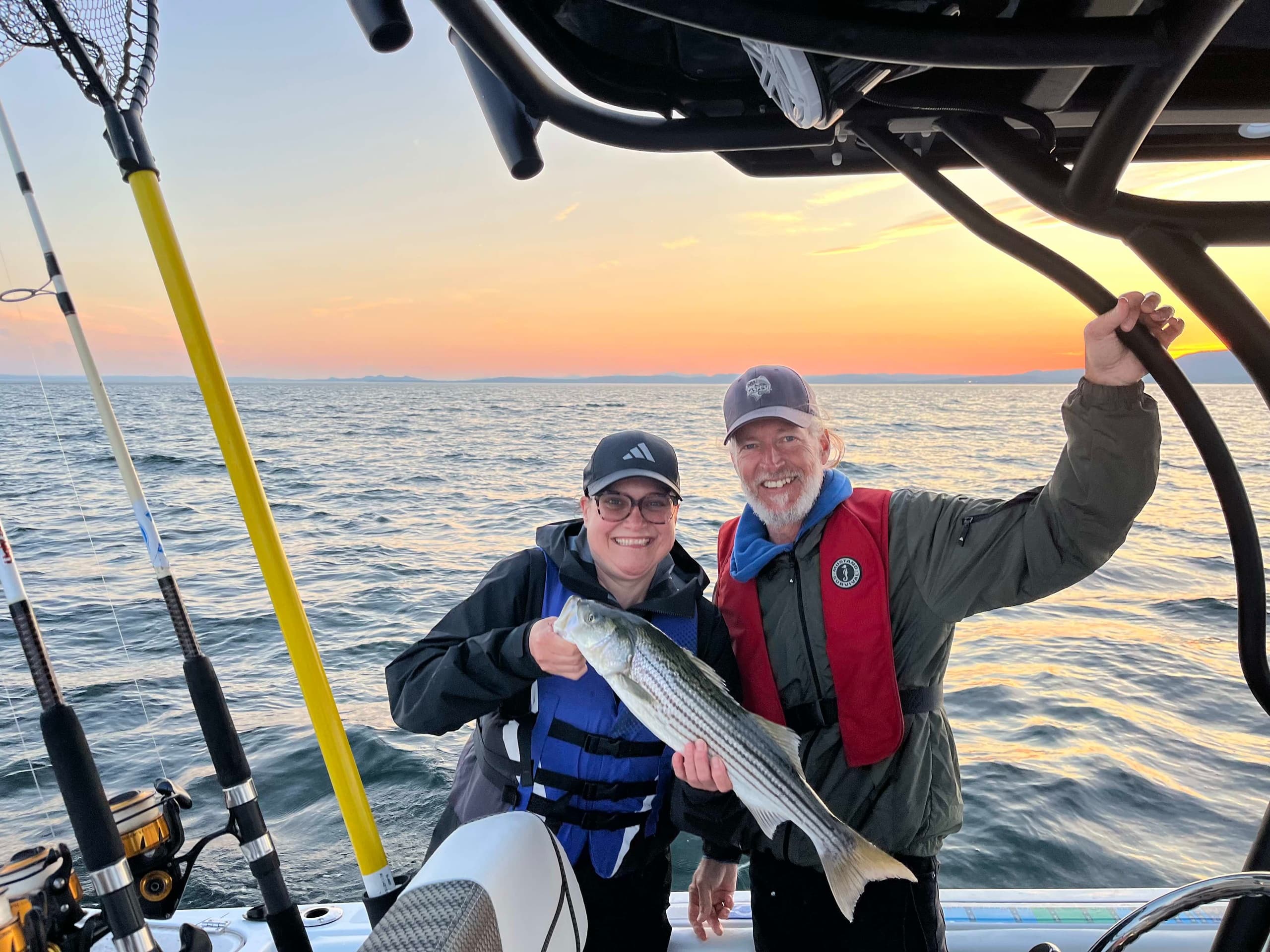 Sunset fishing trip couple holding striped bass on open ocean