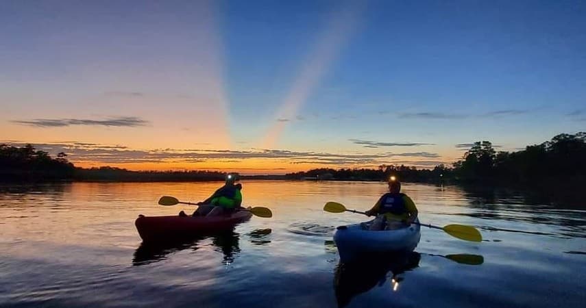 Two kayakers paddling at sunset on a calm lake