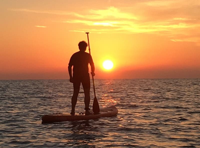 Paddleboarder silhouetted at golden sunset on calm Mediterranean