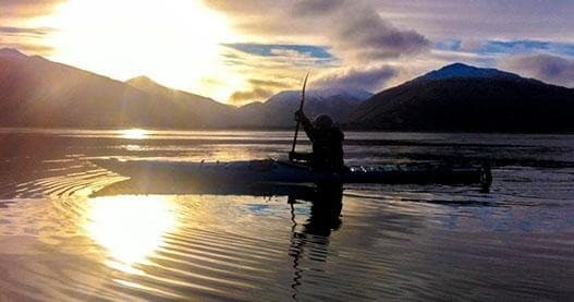 Kayaker silhouetted against bright sunset reflected across glassy water