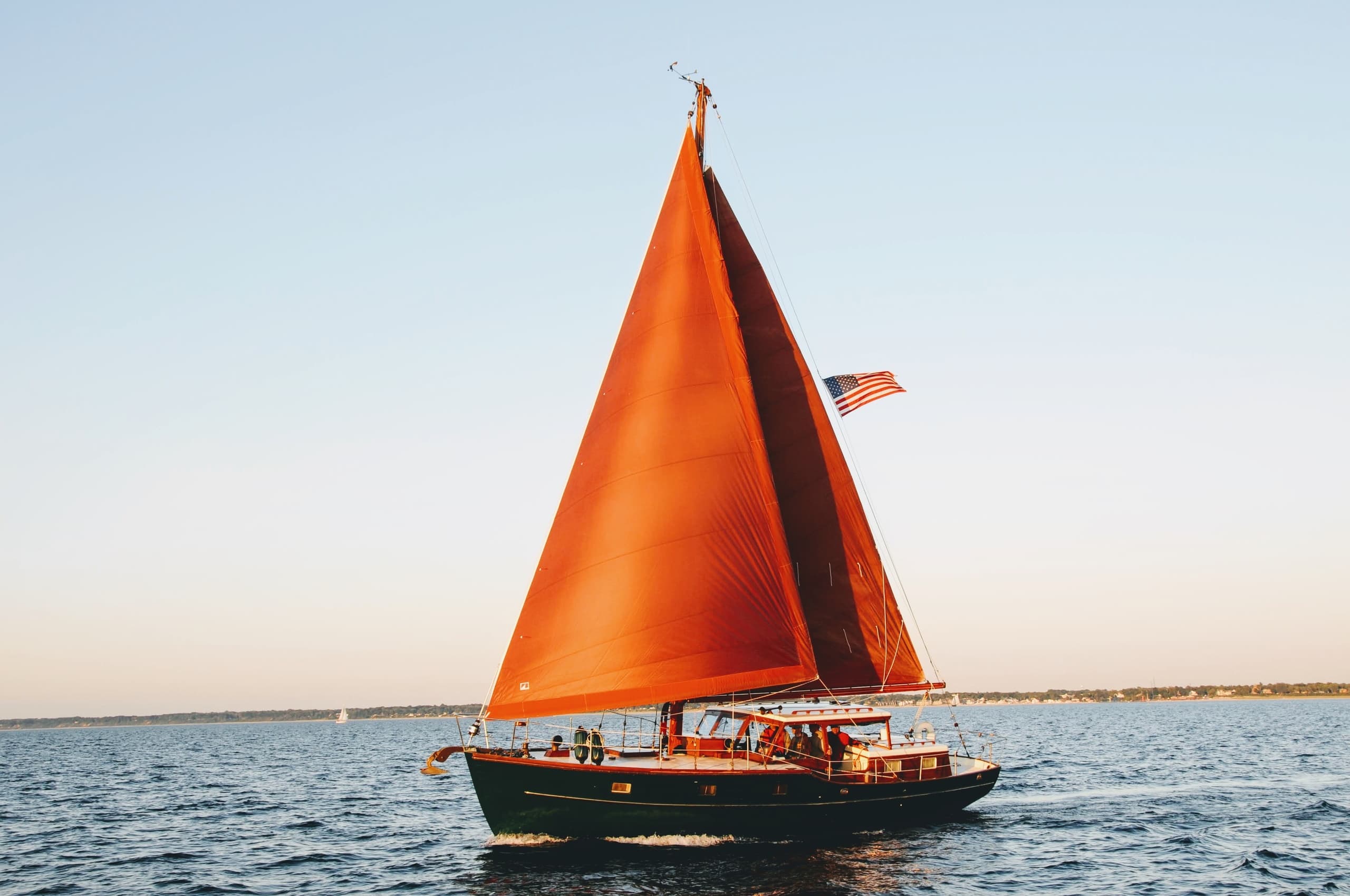 Sailboat with vivid orange sail cruising on calm lake waters