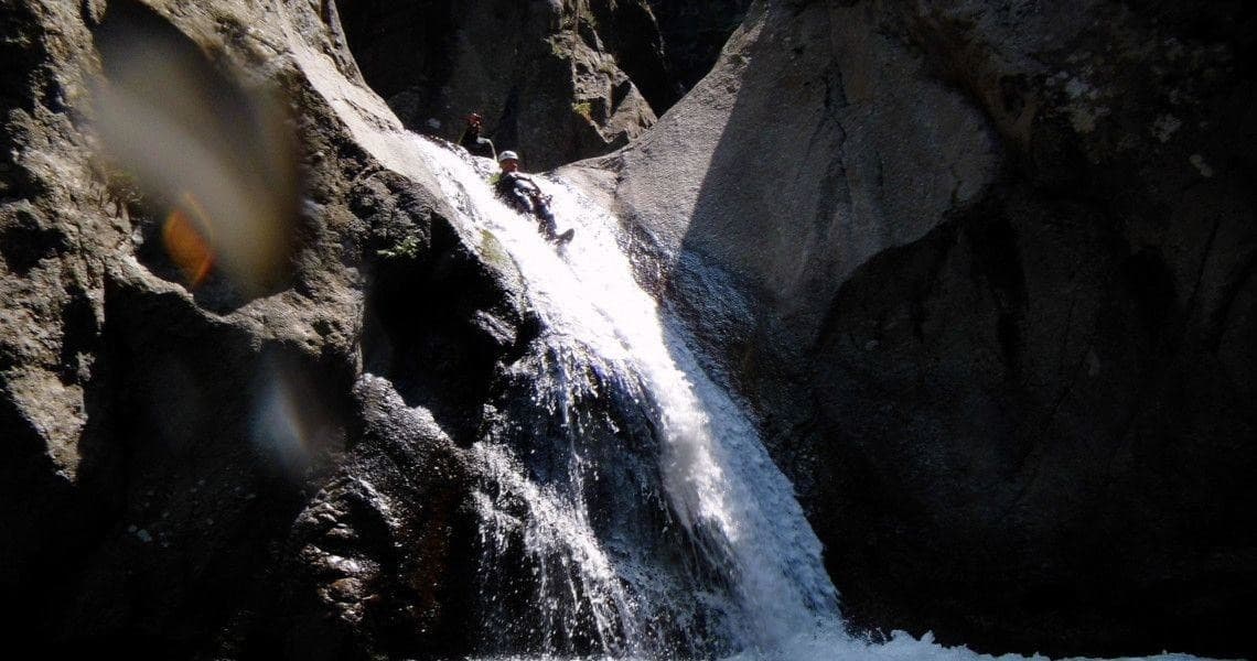 Waterfall cascading through rocky canyon in sunlit mountain gorge