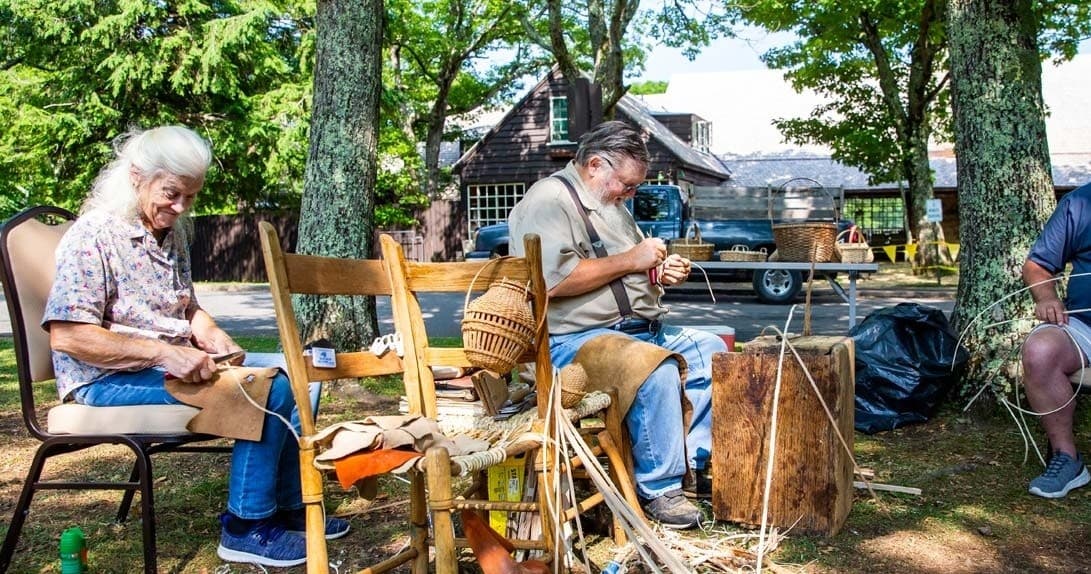 Artisans crafting outdoors at folk festival under shade trees