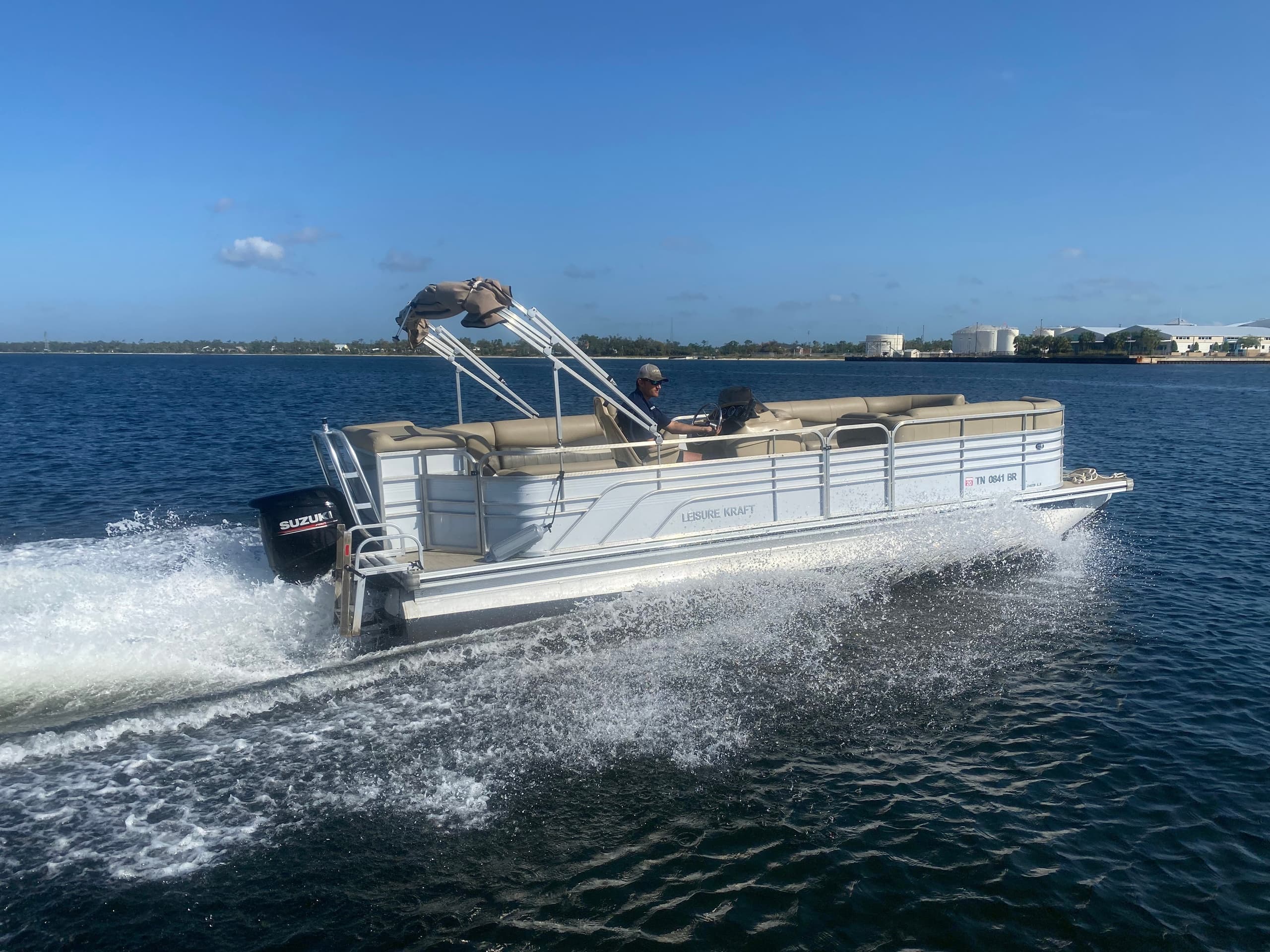 Silver pontoon boat speeding across coastal bay under blue sky