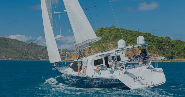 White sailboat gliding past green Whitsunday island coastline