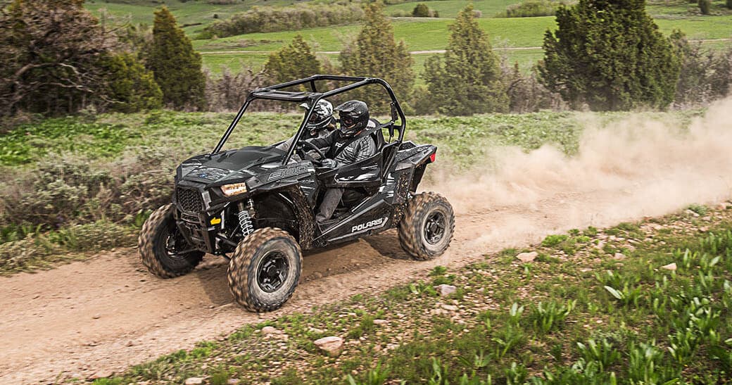 UTV racing along dusty country trail through green fields