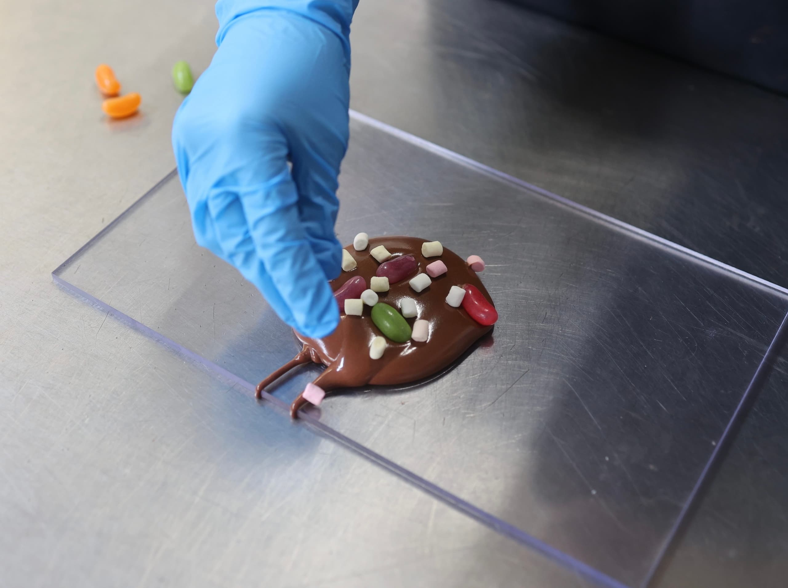 Gloved hand decorating chocolate pieces on workstation tray