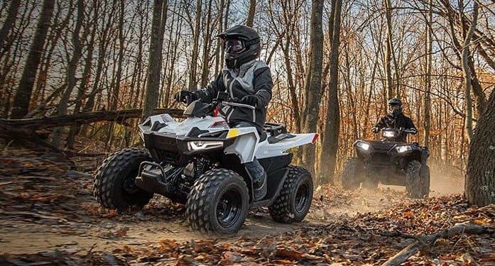 Two ATVs riding through autumn forest trail kicking leaves